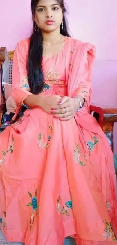 Woman in coral dress sitting elegantly in a decorated room.