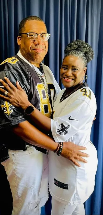 Stylish couple in jerseys with blue curtain backdrop.