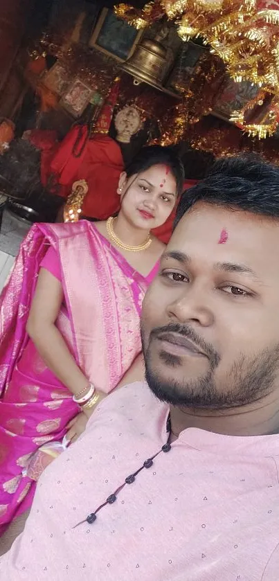 Couple in pink attire posing gracefully in traditional setting.