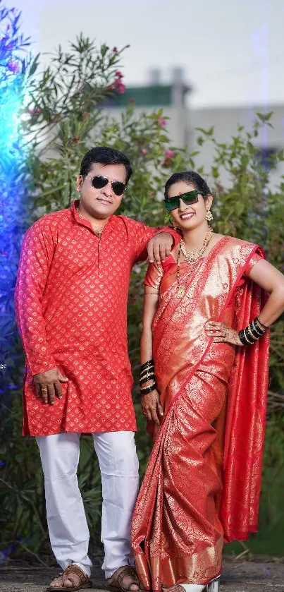 Elegant couple in traditional red attire posing outdoors.