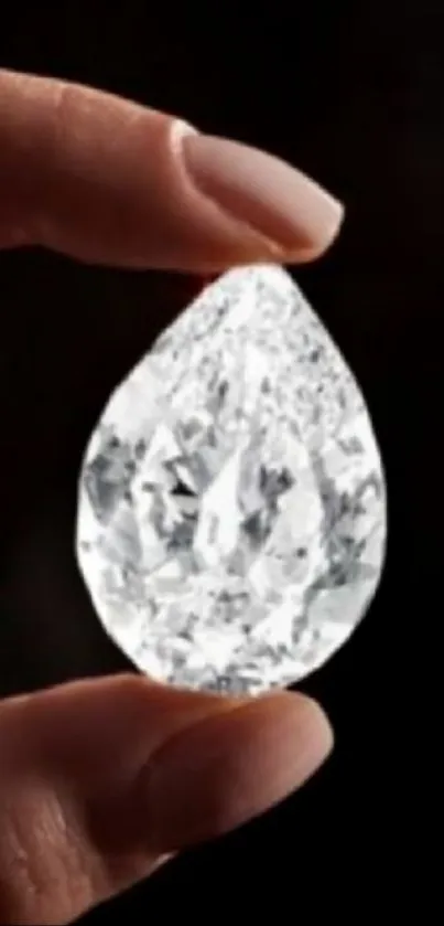 Close-up of a crystal diamond held in hand against dark background.