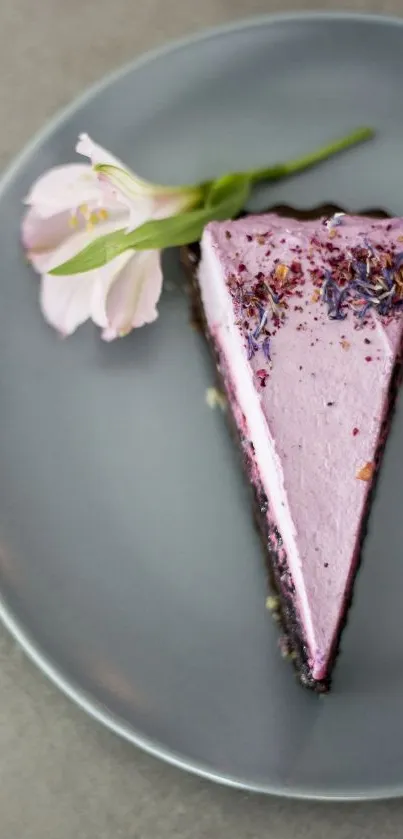 Elegant pink cake slice garnished with flowers on a gray plate.