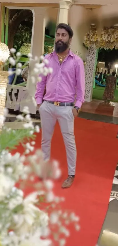 Stylish man at elegant event with red carpet and floral decor.