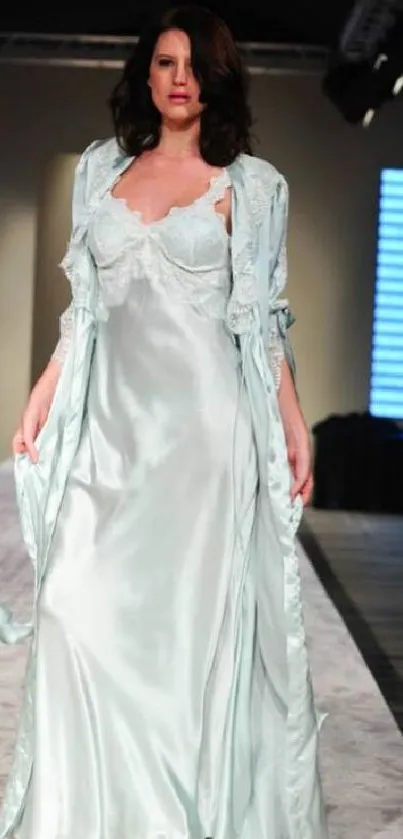 Fashion model in mint green satin gown on runway.