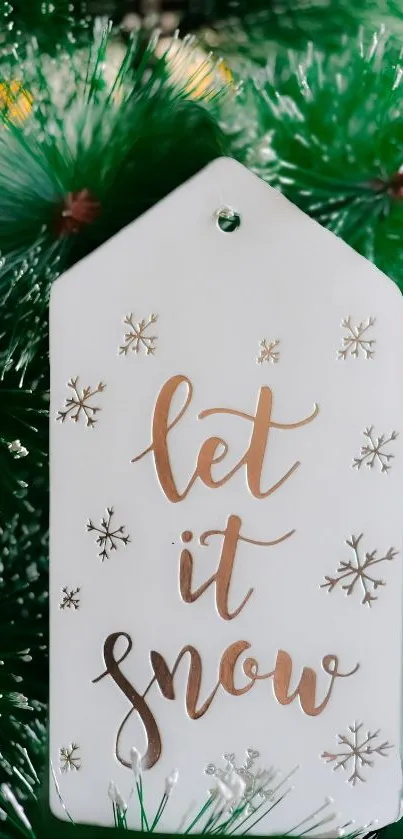 Elegant 'Let it Snow' tag with gold script on green pine background.