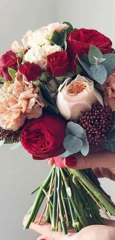 Bouquet of red roses and pink carnations held in hands.