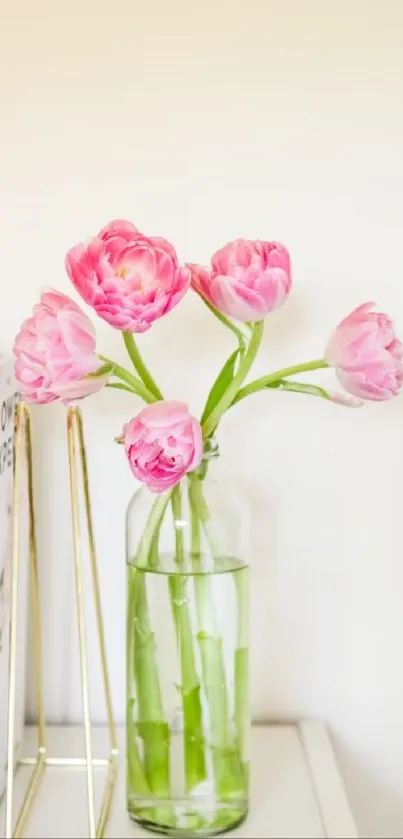 Elegant pink tulips in a clear vase on a white shelf, with books nearby.