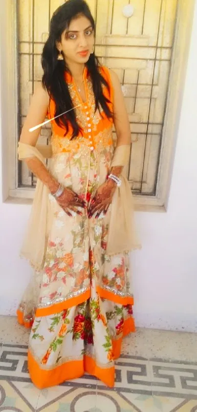 Woman in a floral dress with orange accents standing indoors.