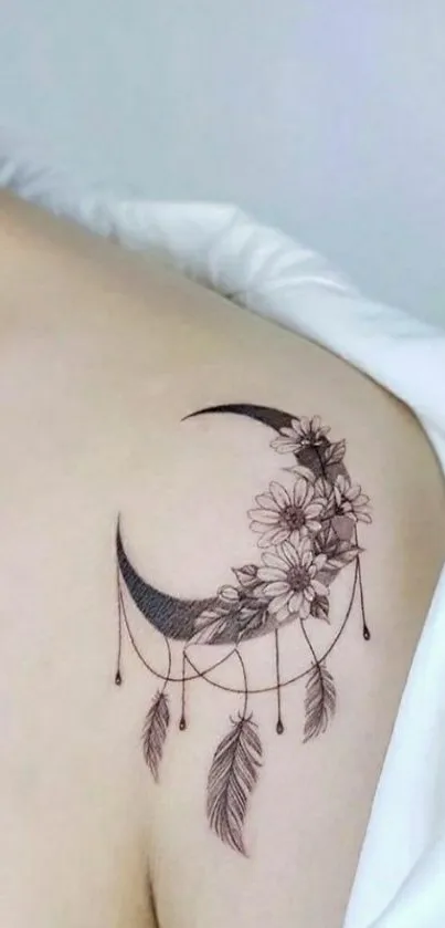 Crescent moon tattoo with flowers and feathers on shoulder.