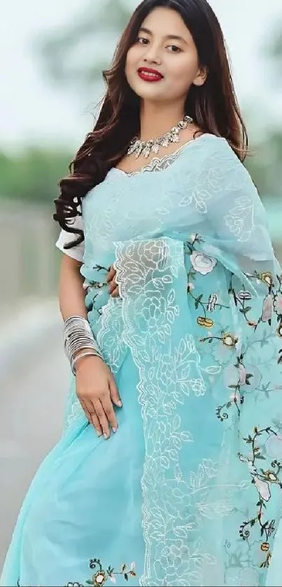 Woman in elegant blue saree with floral embroidery stands gracefully.