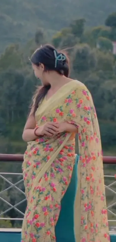 Woman in floral saree with green scenic backdrop.