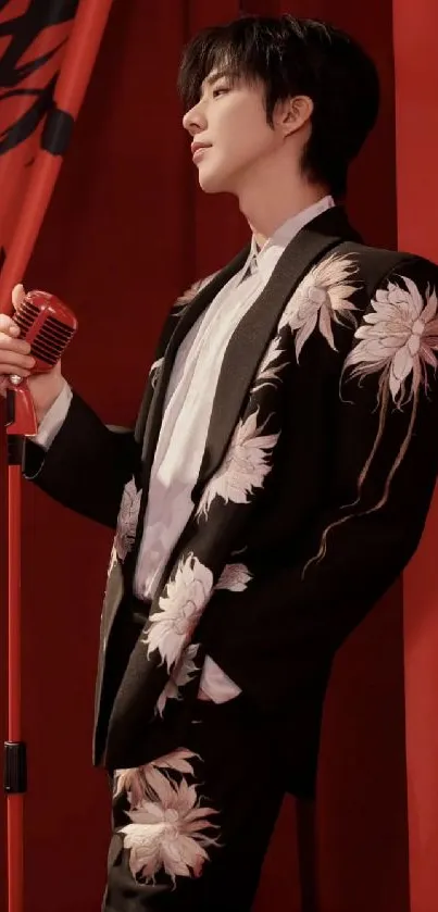 Man in elegant floral suit with red background and microphone.