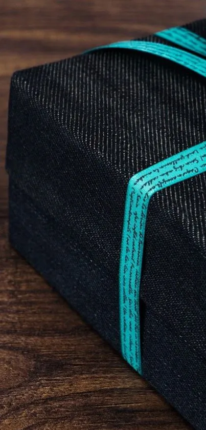 Dark gift box with turquoise ribbon on wooden surface.