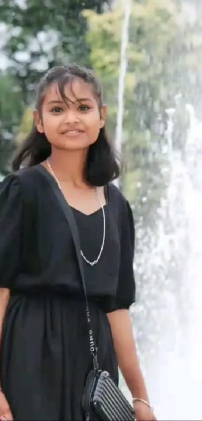 Girl in black dress standing by a fountain.