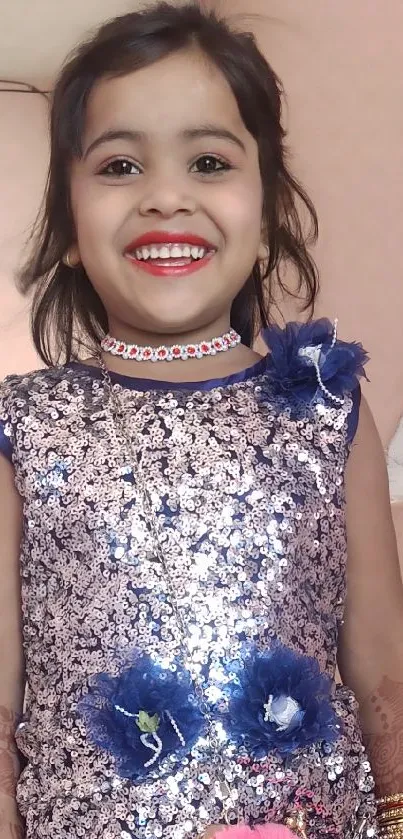 Young girl in a blue sparkling dress with a bright smile and pink accessory.