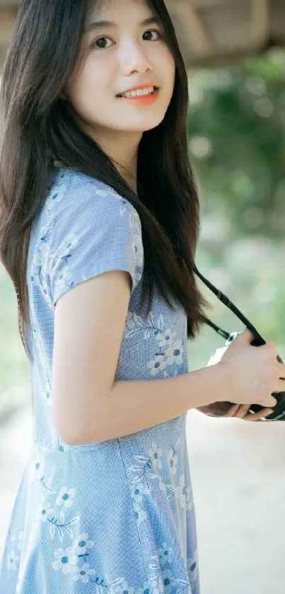 Young woman with camera in blue floral dress outdoors.