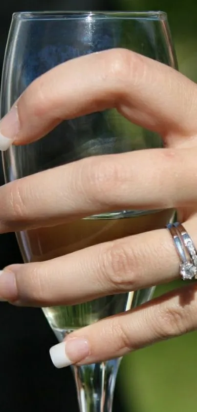 Hand with ring holding a wine glass in an elegant setting.