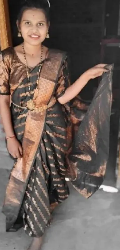 Woman in a gold and black saree standing gracefully.