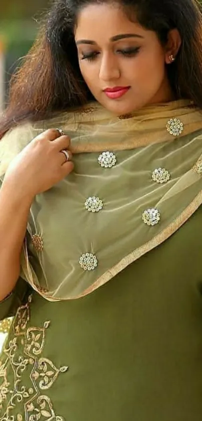 Woman in elegant green attire with embroidered scarf.