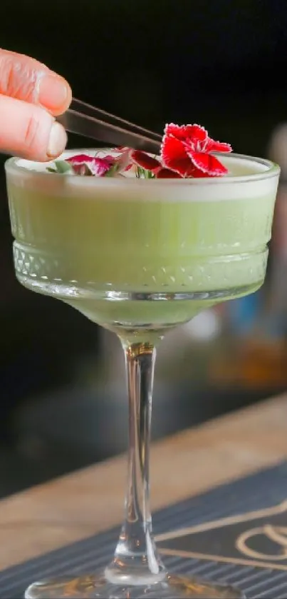 Green cocktail in glass with red flower garnish