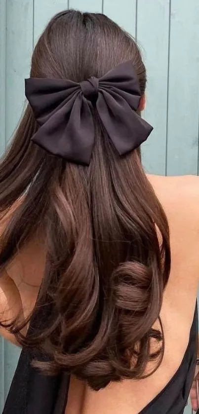 Woman with sleek hair and a black bow against a mint background.