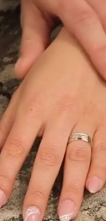 Elegant hand with a ring against a textured stone background.