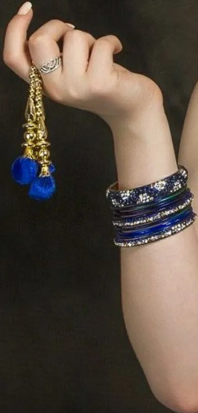 Elegantly adorned hand with blue and gold jewelry on a dark background wallpaper.