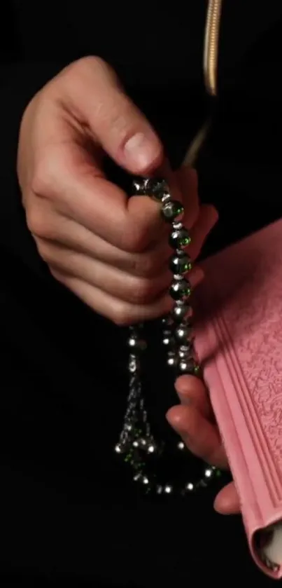 A hand holds prayer beads and a pink book.