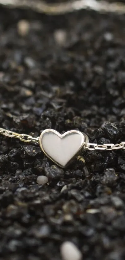 Heart-shaped pendant on chain over dark pebbles.