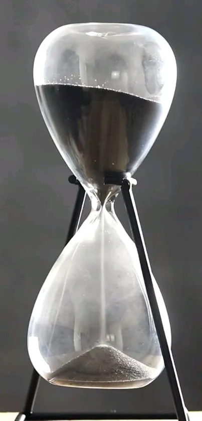 Elegant hourglass with black sand on gray background.