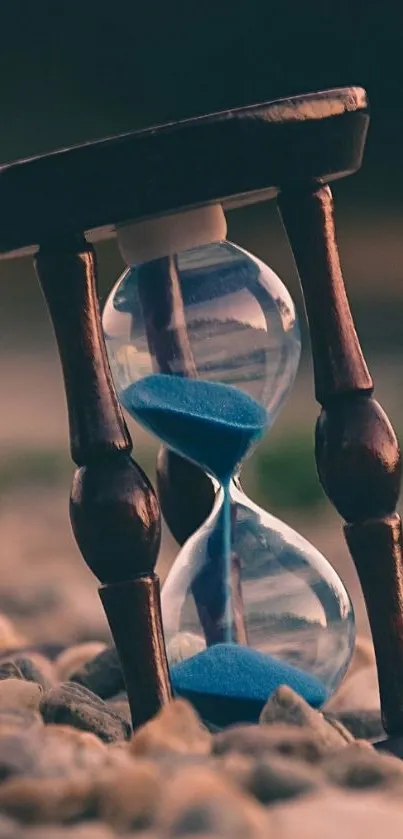 Elegant hourglass with blue sand on pebbles.