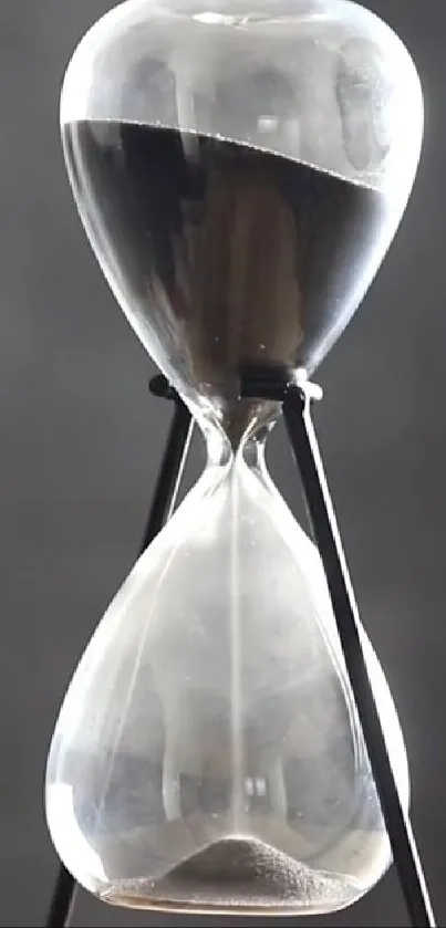 Elegant hourglass with black sand on a dark gray background.