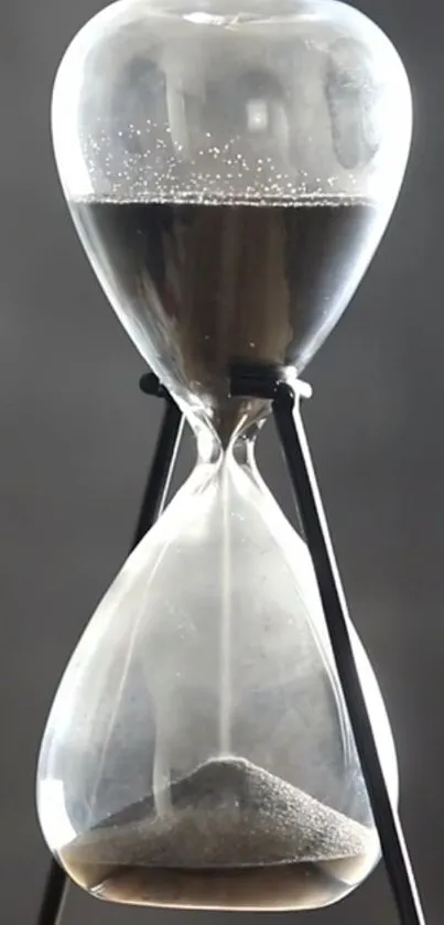 Elegant hourglass with sand on a gray backdrop.