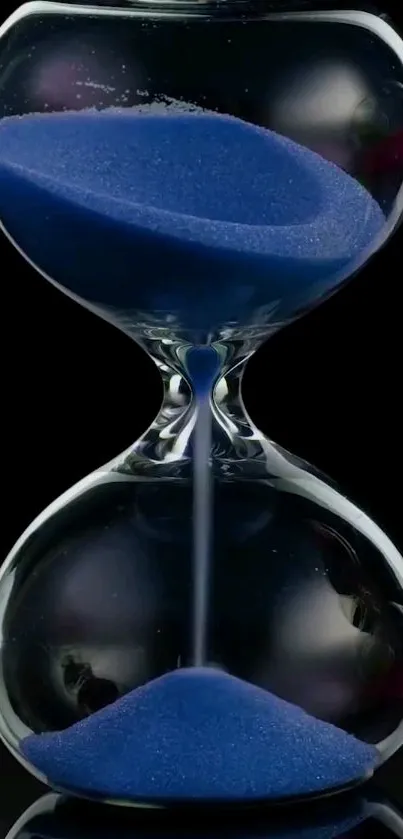 Elegant hourglass with blue sand on black background.