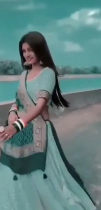 Woman in elegant Indian dress by a serene river with a teal sky.