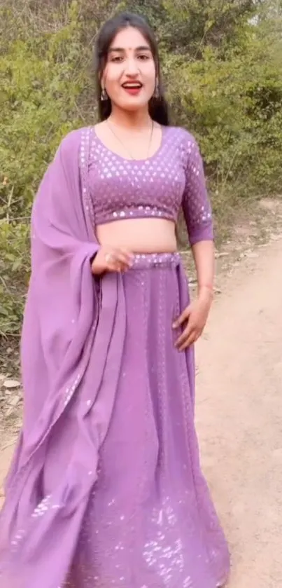 Woman in lavender traditional outfit standing outside with green foliage.