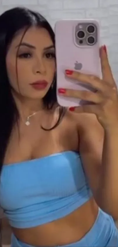 Woman taking a stylish mirror selfie with smartphone, wearing blue outfit.