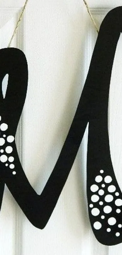 Black letter 'M' art with white dots on a textured wall background.