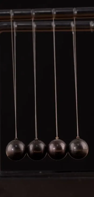 Newton's cradle with four black spheres on a black background.