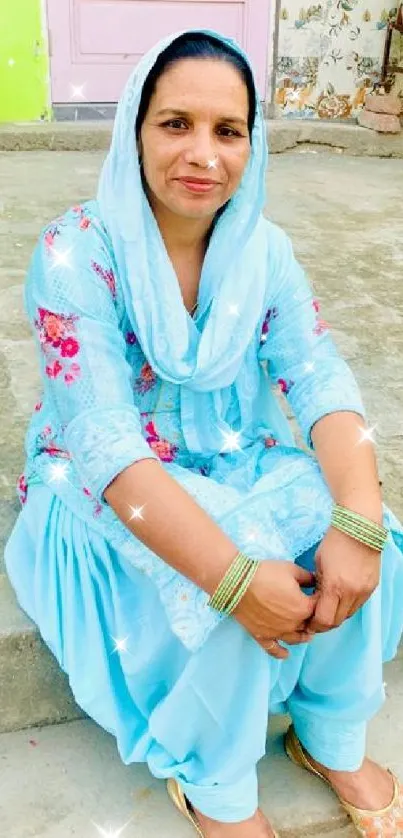 Lady in light blue traditional attire sitting outdoors.