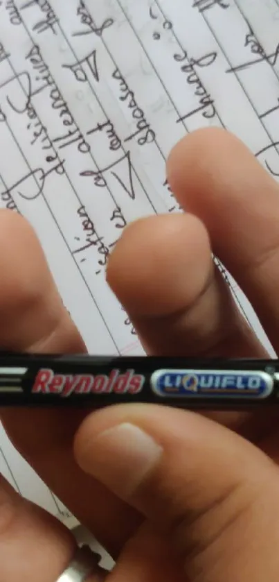 Close-up of hand holding a black pen with notebook in background.