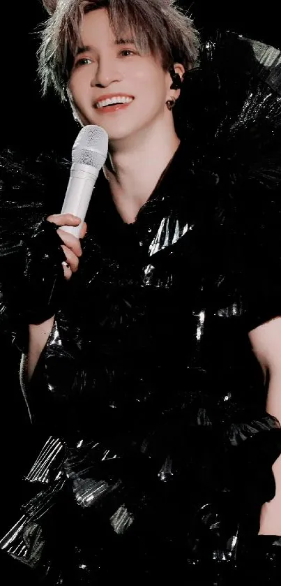 Performer in elegant black outfit with microphone against black background.