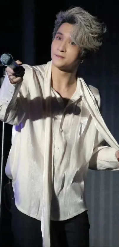 Artistic performer on stage with microphone in white shirt.