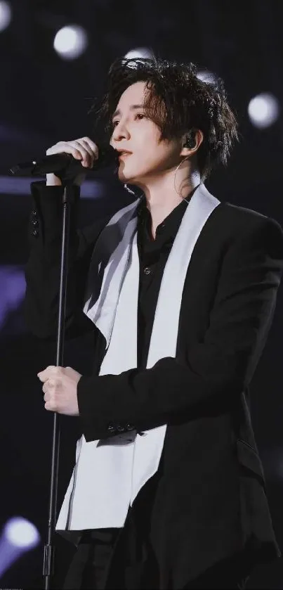 Performer in black suit with a white scarf on stage, captured in elegant style.