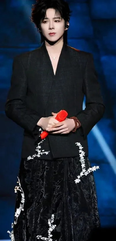 Stylish performer holding a red microphone on stage in elegant attire.