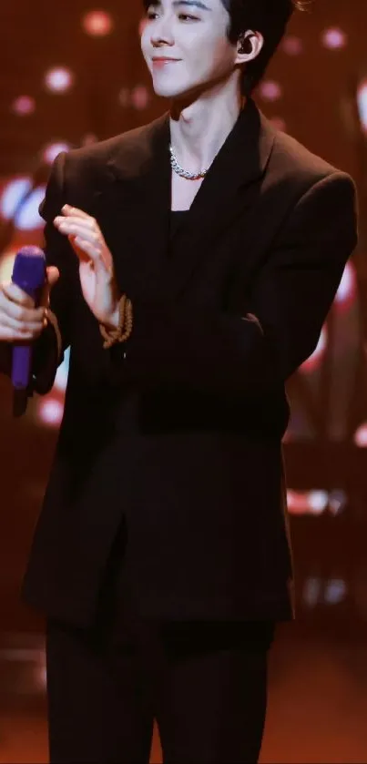 Elegant performer in a black suit holding a microphone on a vibrant stage.