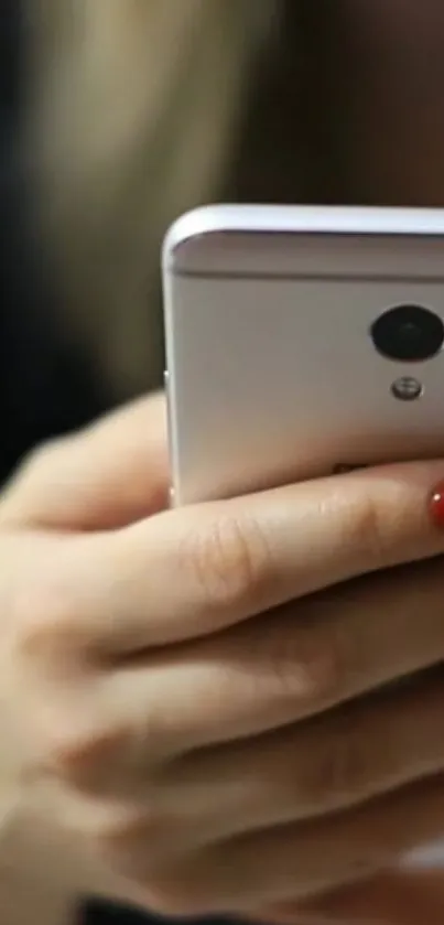 Hand holding a white smartphone with red nails.