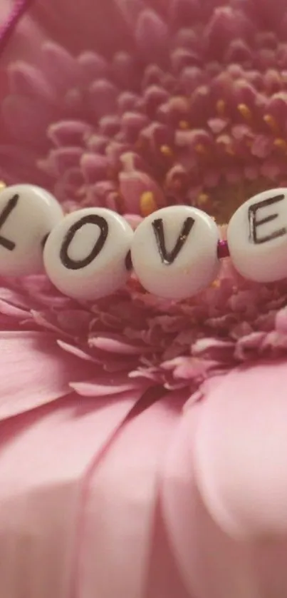 Pink flower with 'LOVE' beads on a mobile wallpaper.