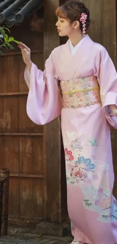 Woman in a pink kimono stands gracefully in a traditional setting.