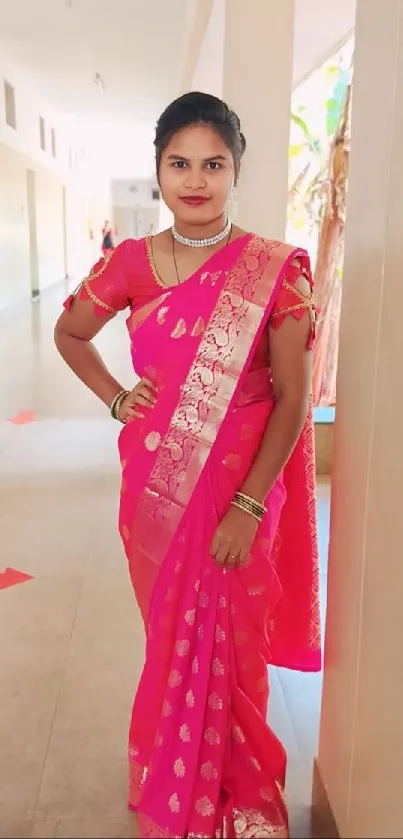 Woman in a vibrant pink saree standing in a hallway.